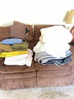 Full view of two stacks of assorted blankets and throws on sofa