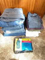 Stack of jeans, t-shirts and packaged raincoat on carpet