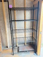Full view of assembled five-shelf black wire rack inside shed