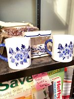 Two blue floral mugs beside boxed miniature saucer set