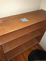 Front and top view of brown veneer bookcase showing three shelves and wear on top surface
