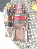 Group shot showing tools, packaged thermometer, barbecue sheet, skewers and smoker box on patio table