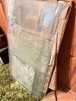 Stack of assorted clear glass panes leaning against wall with newspaper wrapping visible