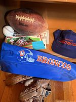Overview showing Wilson football, baseball, Denver Broncos cap, cooler bag, keychain and stack of cards