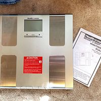 Top view showing LCD screen, control buttons, metallic footpads, and included manual