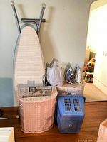 Ironing board, holder, two irons, two hampers and blue basket grouped together
