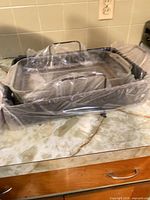 Stacked handled metal roasting pans wrapped in plastic