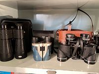 All three binoculars with their respective cases and straps on shelf