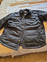 Black insulated button-front jacket laid flat on bed