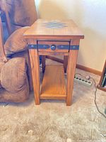 Full view of oak mission style end table beside chair showing drawer front, metal accents and lower shelf