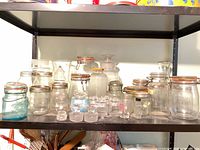 Assorted clear and aqua glass jars and loose stoppers on shelf