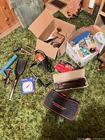 Lot overview showing boxed tools, utility light, caulking gun, thermometer, hose adapter, table legs and hardware