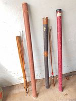 Overall view of two bamboo rod sets, three tubes and fabric sleeve leaning against wall
