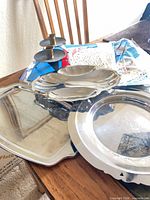 Stack of assorted metal trays, candlestick pair, packaged doilies