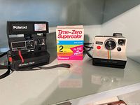 Both Polaroid cameras and boxed film on shelf