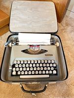 Typewriter inside open carrying case showing keys, ribbon area and gray body