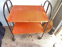 Front view of orange two-tier bar cart with black frame and casters