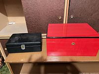 Black faux-leather travel humidor beside red desktop humidor, closed view