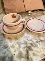 Cup stacked on saucer with side plate, showing red band and crown design