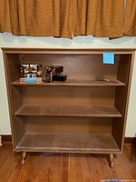 Front view of brown three-shelf bookcase, empty except for excluded items