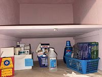 Shelf with blue and white baskets containing toothbrush packs, mouthwash, IcyHot sleeve, hydrogen peroxide, Band-Aid boxes, lotions and other first-aid items