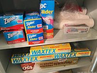Shelf with Ziploc boxes, Waxtex boxes, Reynolds paper, disposable cups and cutlery visible