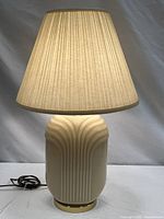 Front view of cream ceramic ribbed table lamp with pleated shade, cord visible