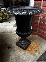 Front angled view of black cast iron urn showing rim detail, fluted body, pedestal base