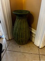 Full view of the green ceramic vase positioned in a corner showing shape and carved pattern