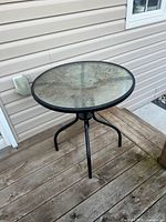Round glass-top metal bistro table on wooden deck