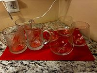 Two tulip motif mugs with four rounded tumblers on red cloth
