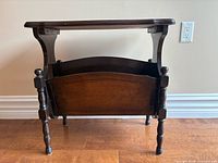 Front view of dark wood side table with integrated magazine rack, showing turned legs and open compartment