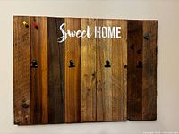 Front view of rustic wooden memo board showing “Sweet HOME” text, six black clips and four coloured push pins