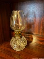 Full view of small clear glass oil lamp on wooden shelf