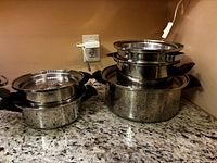 Two stacks of stainless steel pots on granite countertop