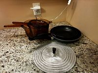 Overall view of saucepan, insert, frying pans and lid on countertop