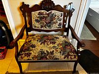 Front view of carved wood bench showing floral upholstered seat and back