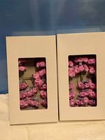two white window boxes showing pink artificial flowers inside
