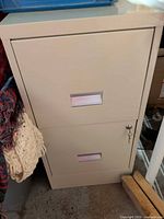 Front view of beige metal two-drawer filing cabinet showing label holders, key in lock