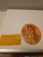 Front of copper disc with painted portrait and note specifying firing instructions