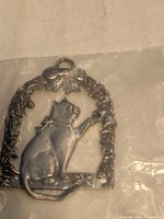Front view of pewter cat ornament in plastic bag