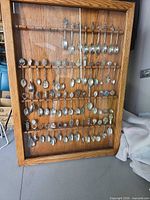 Full view of oak framed glass-front spoon rack with multiple souvenir spoons displayed