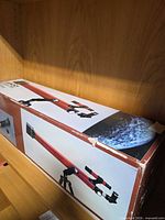 Closed cardboard box showing Tasco red telescope imagery