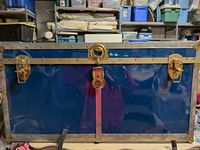 Front view of blue metal trunk with brass hardware and wood slats