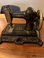 Left side view of miniature hand-crank sewing machine showing overall form and decals