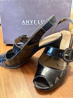 Both shoes showing patent leather finish and slingback design against Anyi Lu box