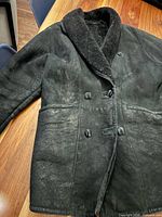Full front view of black shearling coat showing double-breasted buttons, collar, pockets