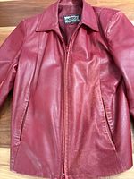 Front view of red leather jacket showing collar, zipper closure, pockets and wear on panels