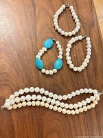 Four bracelets arranged on wood surface: two single-strand pearls, one triple-strand pearls, one pearl & turquoise bead