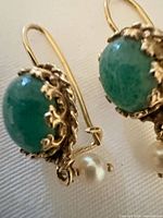 Close-up of green cabochon earring showing setting and faux pearl